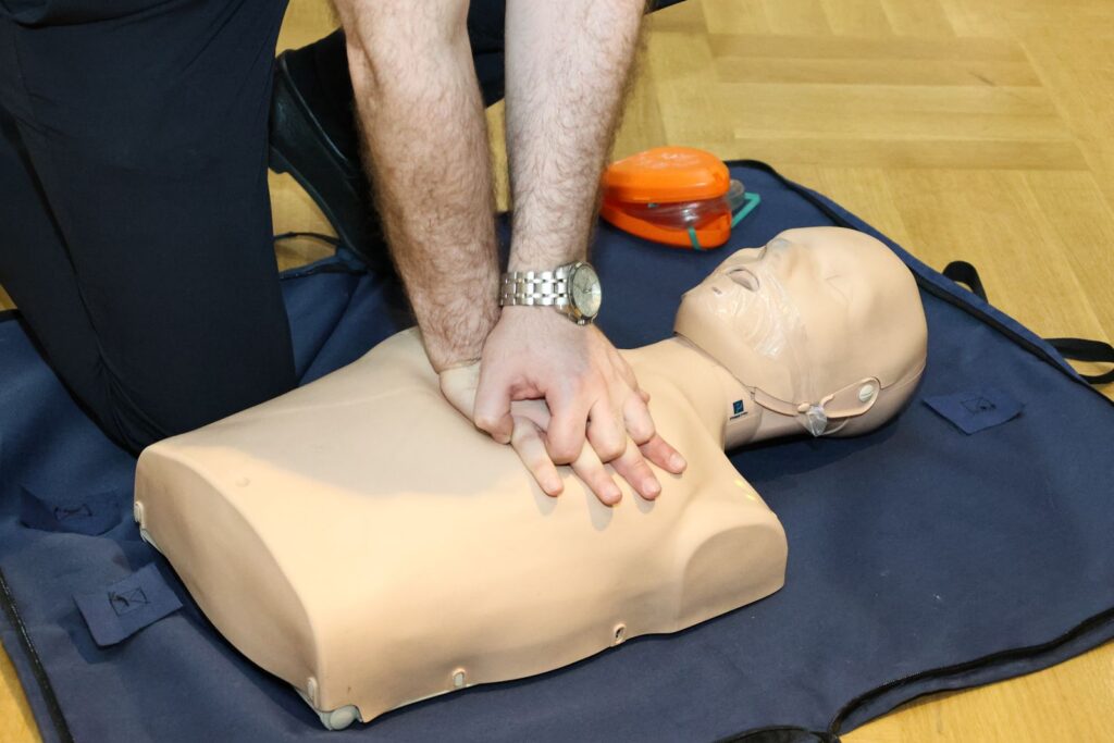 Hands performing chest compressions on a CPR manikin during emergency first aid at work training