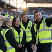 Steward supervisor briefing a stewarding team beside the pitch at a football ground